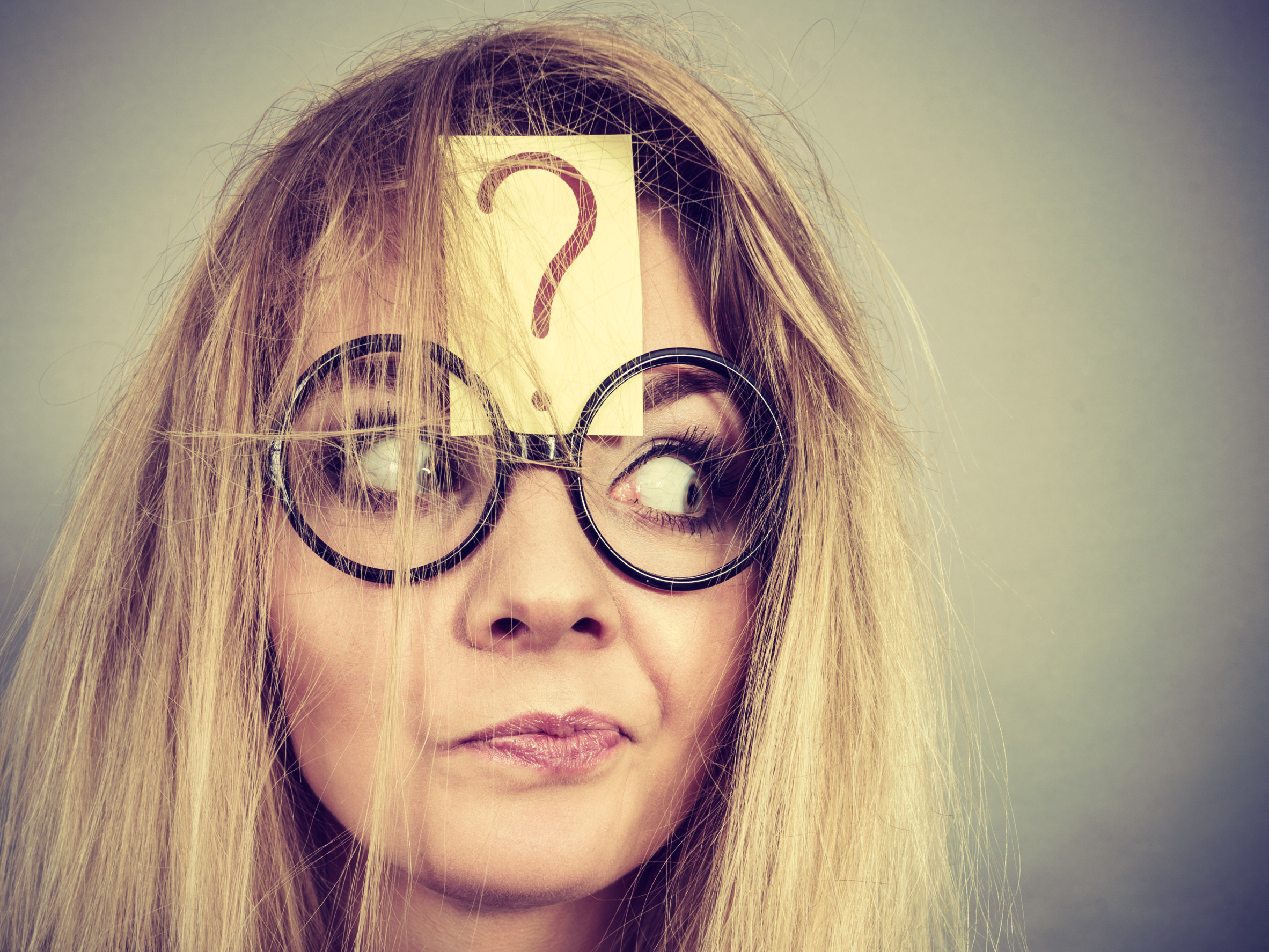 a white woman's face with blonde hair and big round glasses with a question mark on her forehead