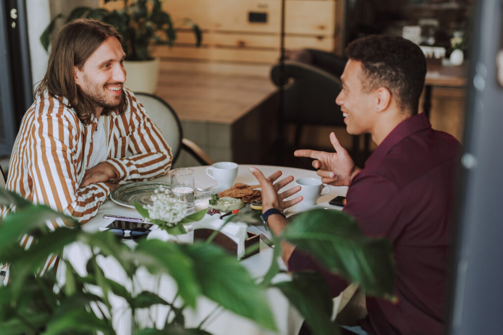 Two young men looking at each other, chatting and laughing in a cafe.